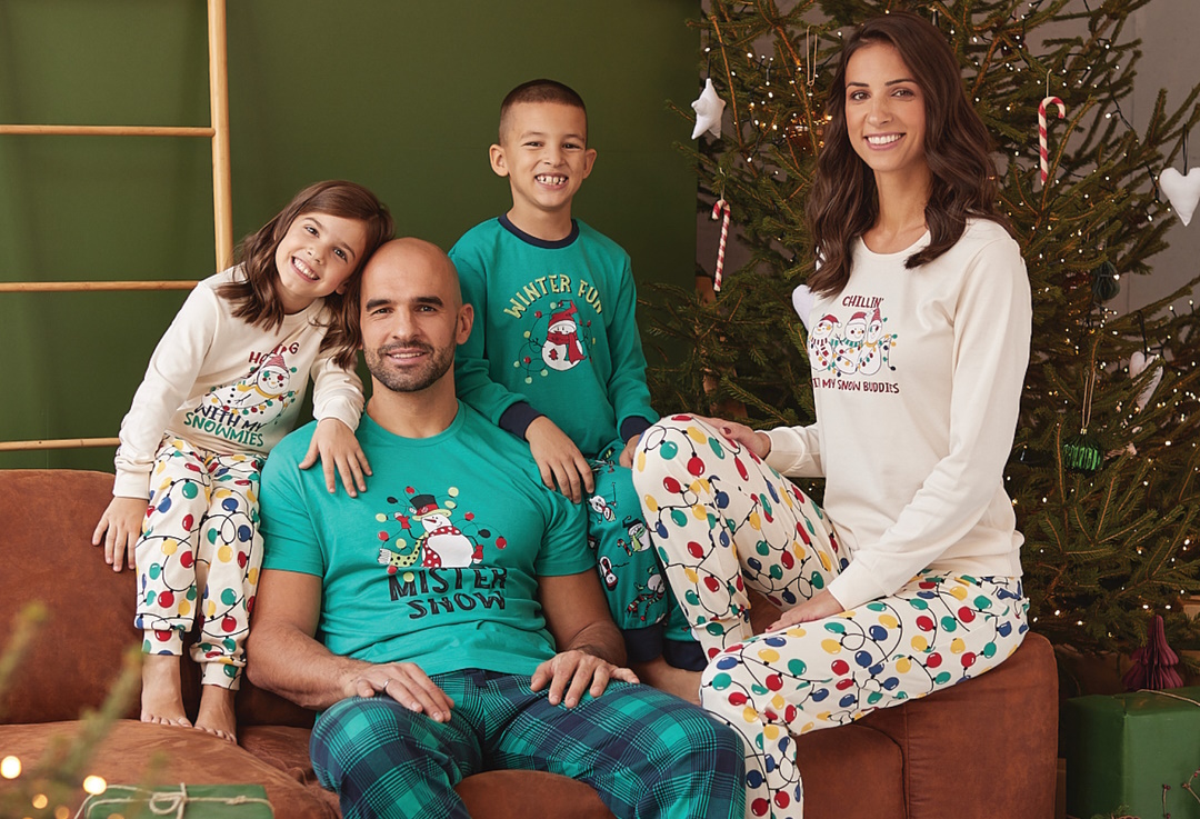 Porodica sedi ispred jeleke u novogodišnjim pidžamama