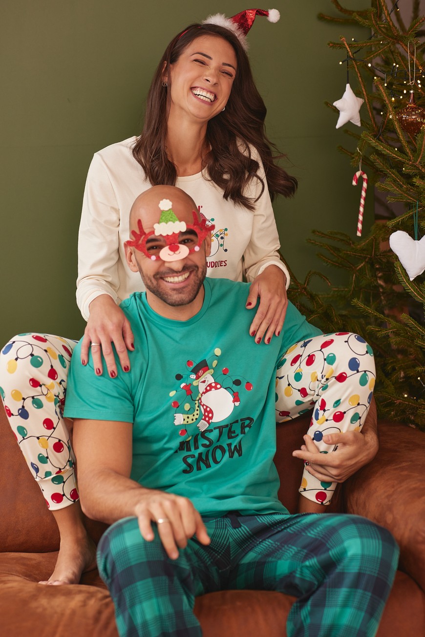 Muškarac i žena u Jasmil novogodišnjim pidžamama za parove, sede ispred novogodišnje jelke